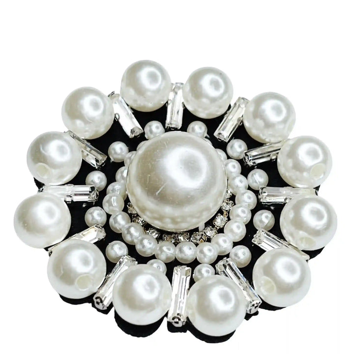 A patch adorned with white pearls arranged in a floral pattern with a larger pearl in the center and small pearl-like beads around it, all attached to a black base.