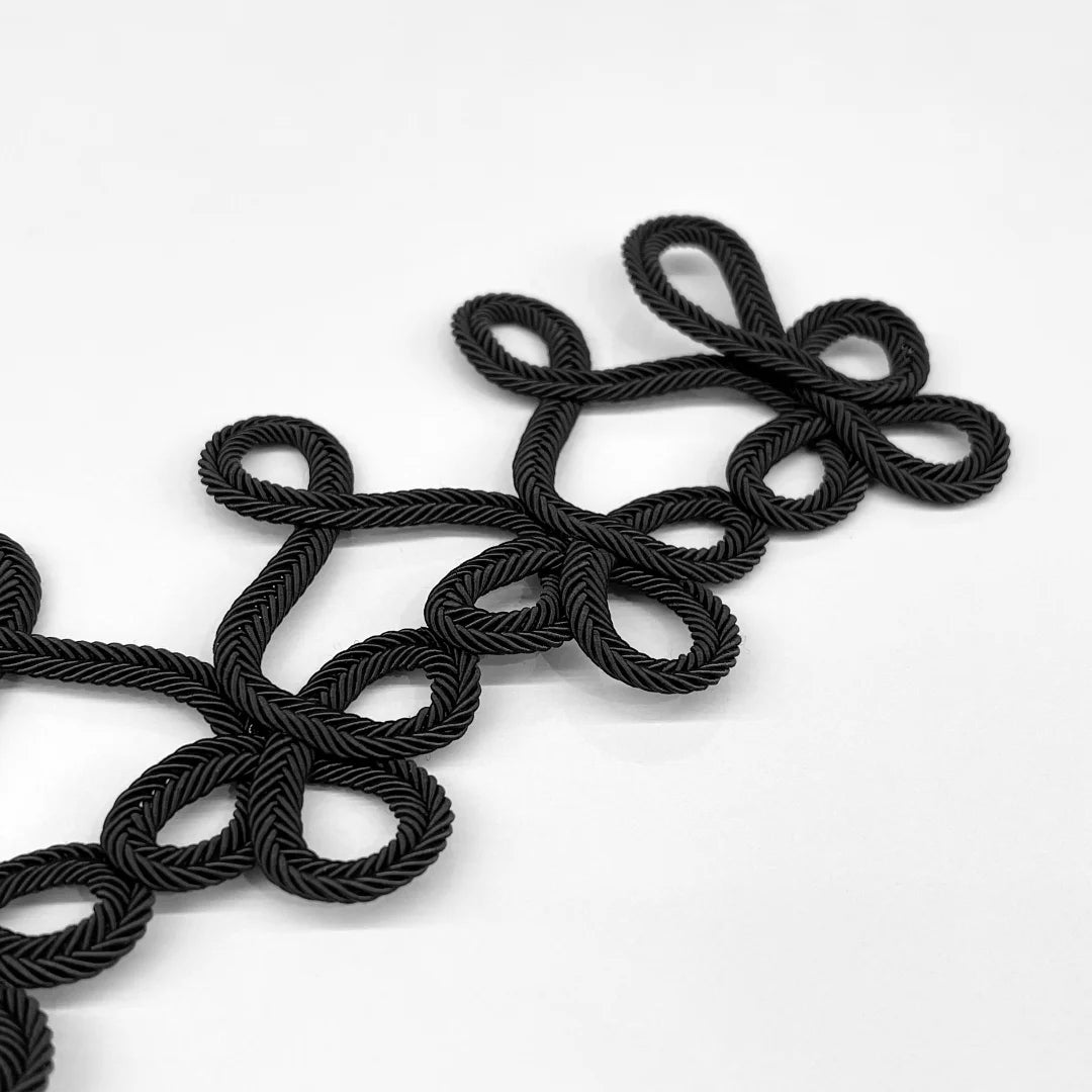 Black braided rope trim with a decorative looped pattern, laid diagonally on a clean white background.