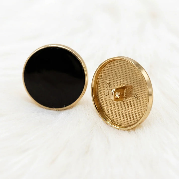 Two black resin gold rim metal buttons standing upright, angled view of the raised gold rim, grid-textured back and shank.