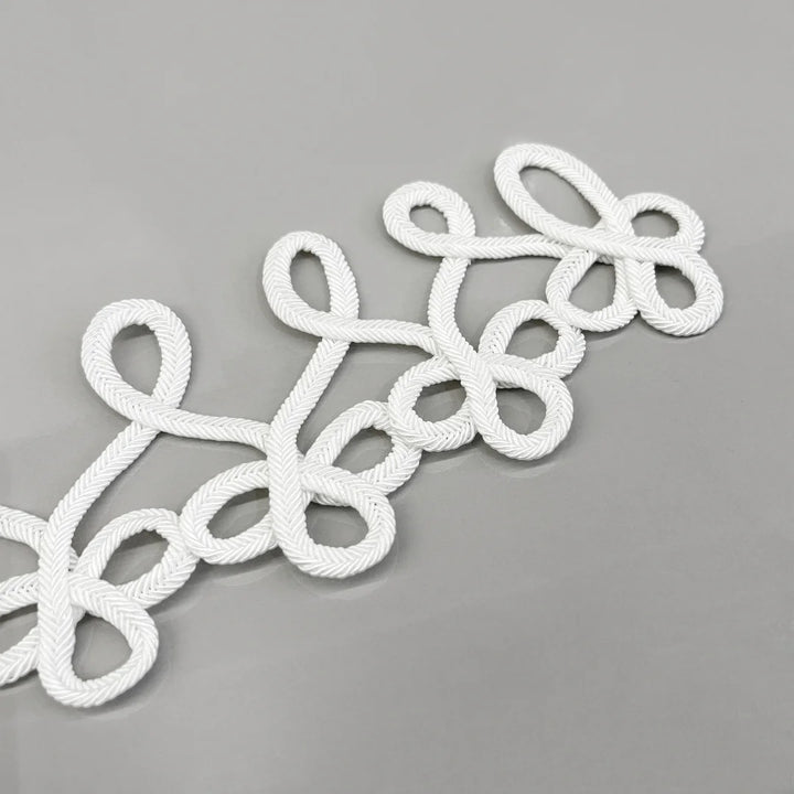 White braided rope decorative trim with an elegant looped pattern, laid diagonally on a smooth gray surface.