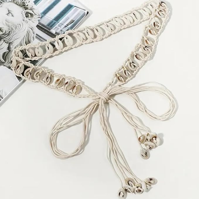 Ani Accessories Womens Belt Beige cowrie shell belt laid out, tied in a simple bow. Ends have shell clusters. Styled with magazine pages.