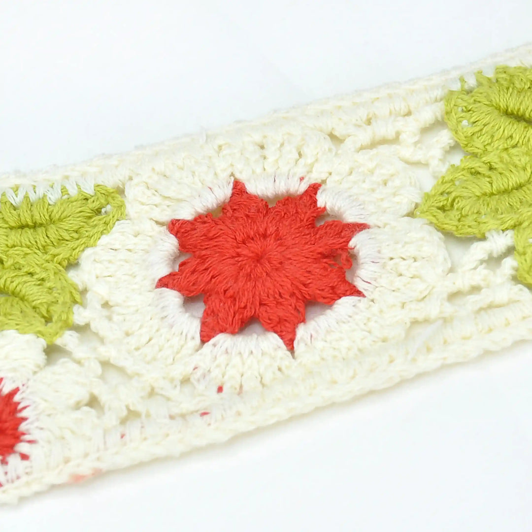 Zooming crocheted lace with red and green floral patterns on a white background
