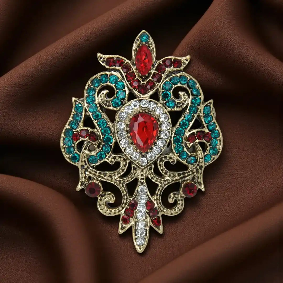 ANI Accessories baroque revival brooch in antique gold with ruby-red teardrop and teal rhinestones on brown satin 
