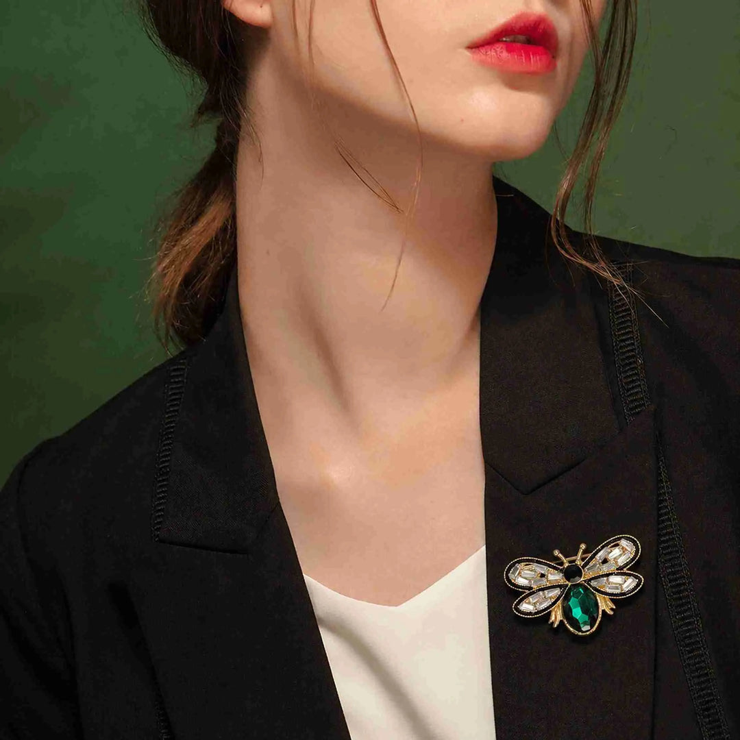 Woman wearing an emerald crystal bee brooch on a black blazer lapel
