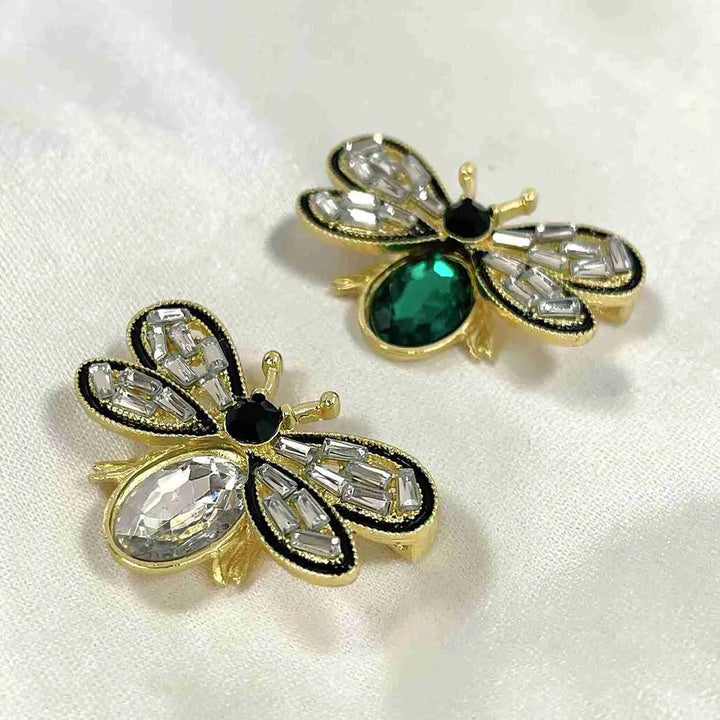 Emerald and white crystal bee brooches on white faux fur with white color background 