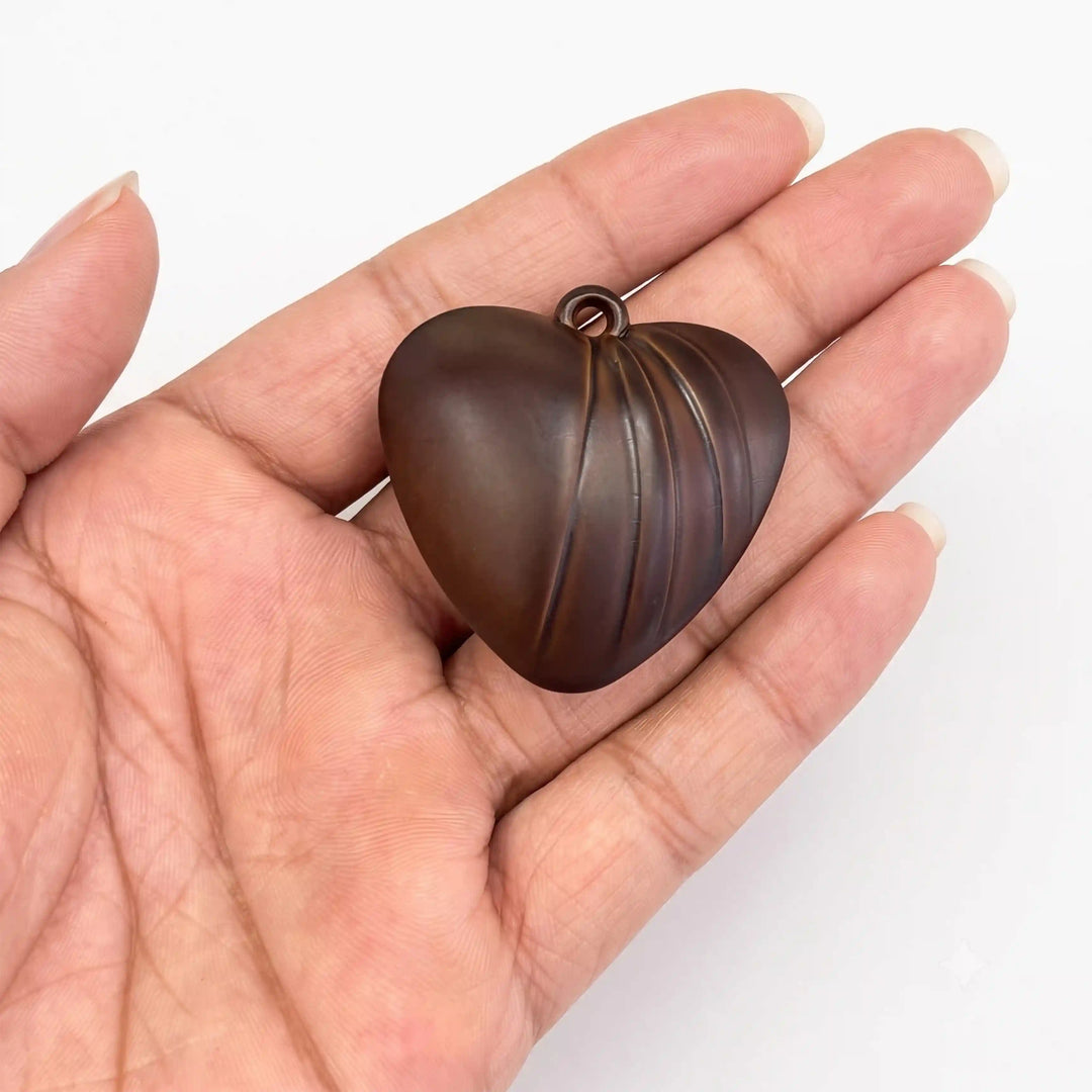 ANI Accessories dark brown fluted heart charm held between fingertips, side view showing puffy shape and thickness with white color background 