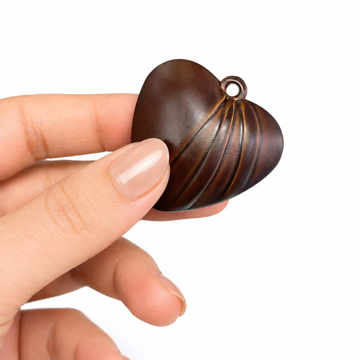 ANI Accessories dark brown fluted heart pendant charm resting in an open palm to show real size, on white background 