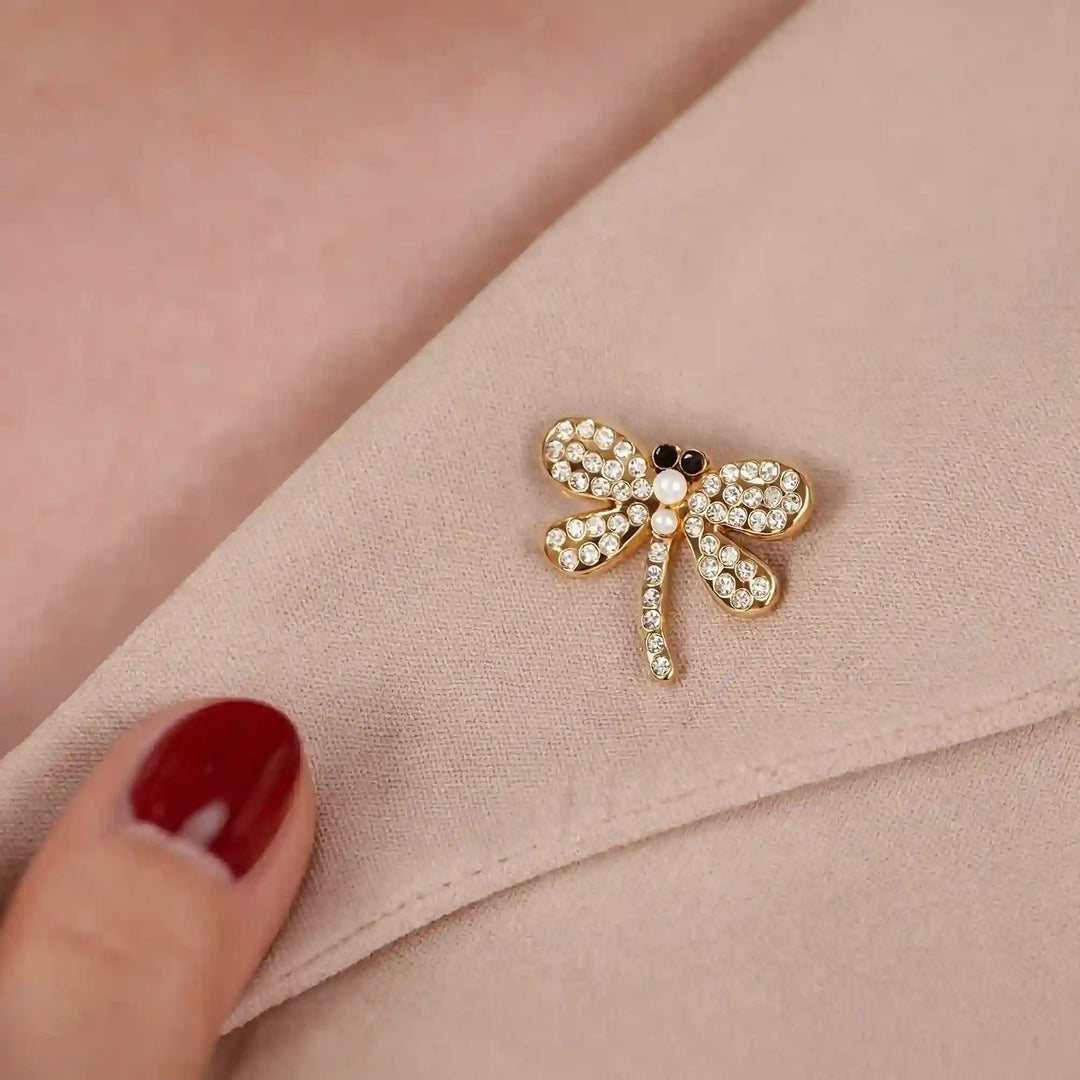 Mini dragonfly lapel pin on a pink blazer held by a woman’s hand 