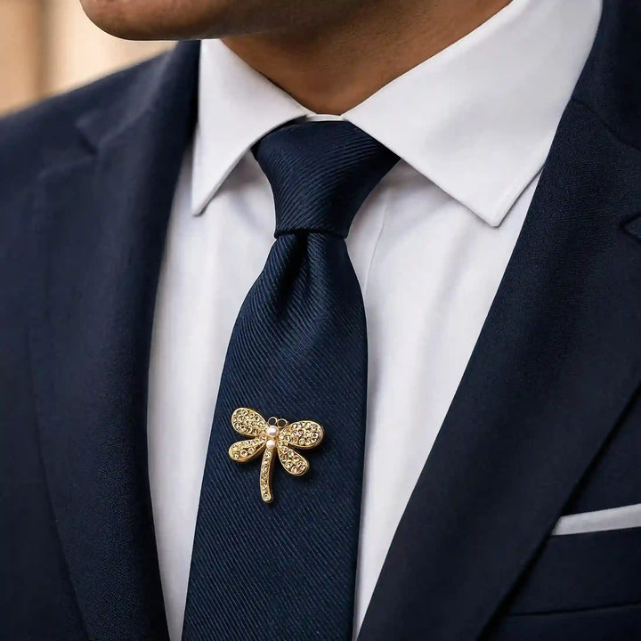 Man wearing a mini gold dragonfly pin on a navy tie with a suit with white color background 
