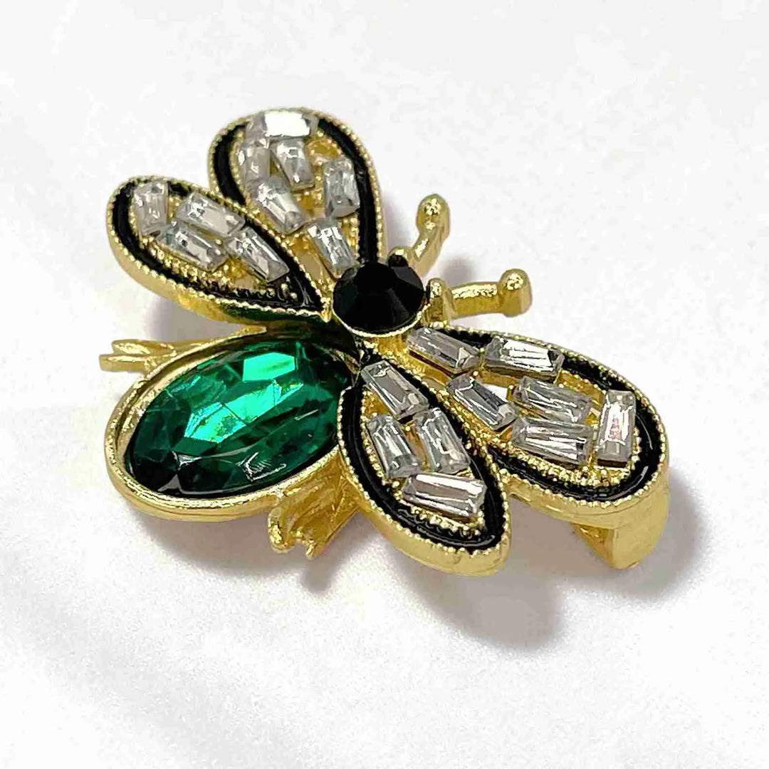 Side view of the emerald crystal bee brooch showing the gold frame with white color background 