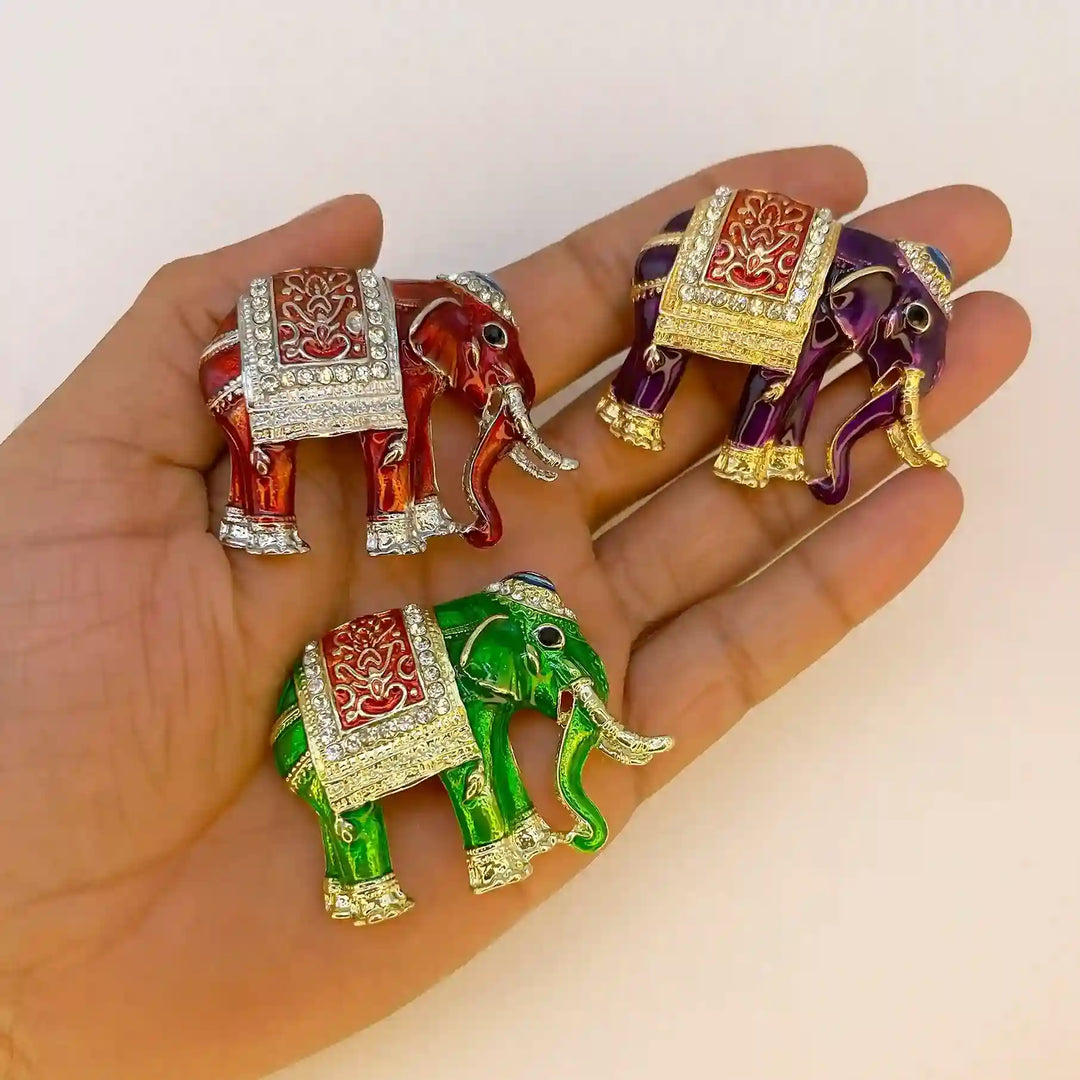 Three enamel elephant brooches held in hand to show their size white color background 