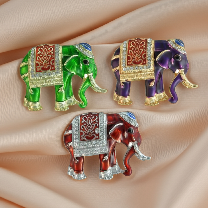 Enamel elephant brooches in red, purple and green with decorated saddle cloth on beige satin 
