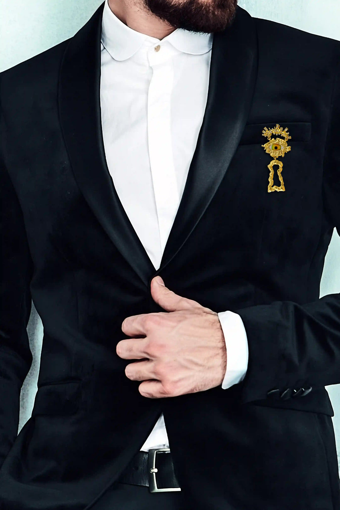 Man wearing a gold eye brooch pin on a black tuxedo lapel with white color background 