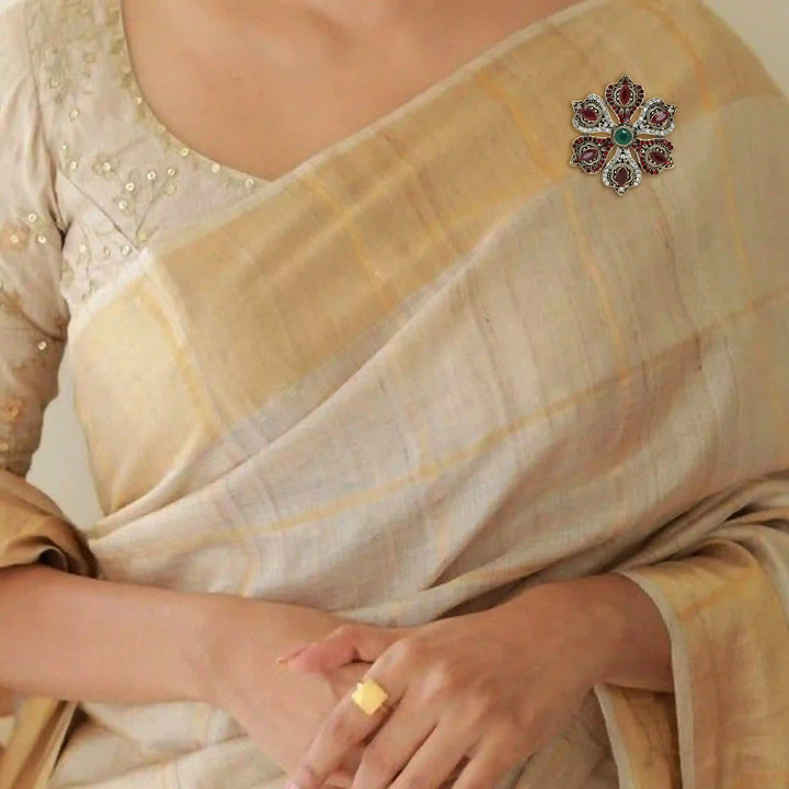 ANI Accessories flower corsage brooch on the shoulder of a cream and gold sareeb with white color background 