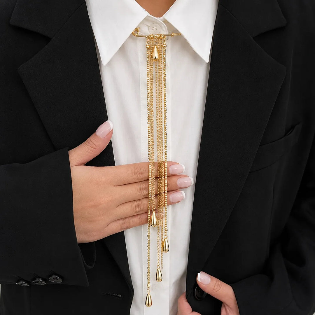 ANI Accessories gold chain tassel brooch worn like a tie at a white shirt collar with a black blazer 
