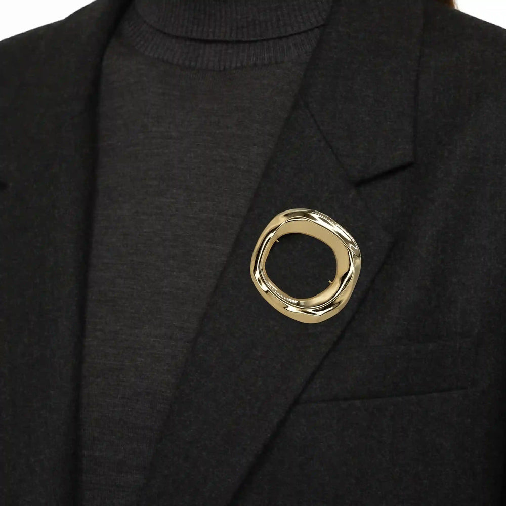 ANI Accessories gold circle brooch pinned on the lapel of a black blazer 