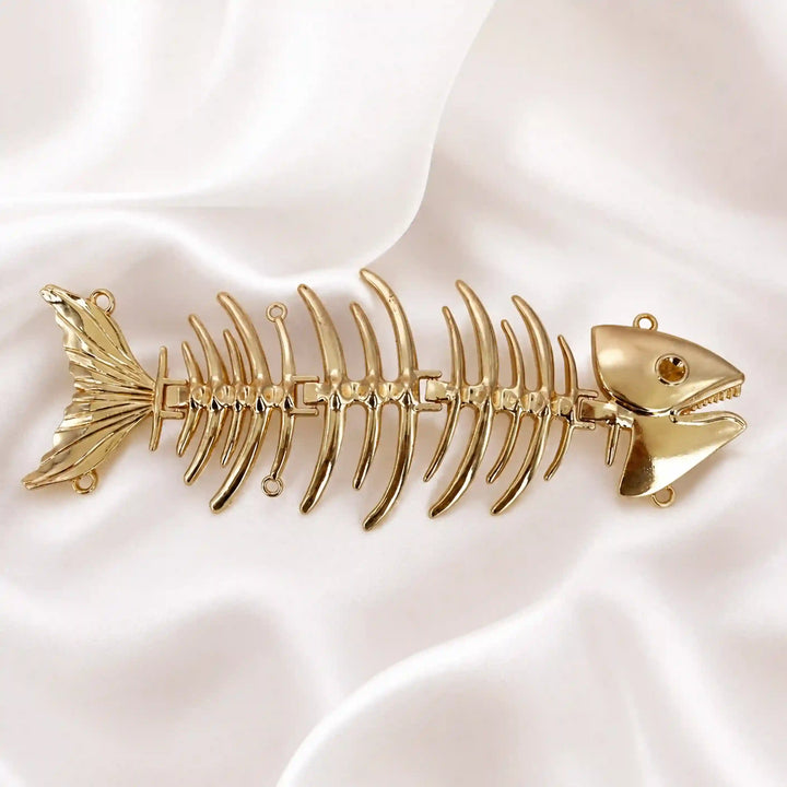 ANI Accessories fish skeleton sew brooch in high-shine gold on white satin 
