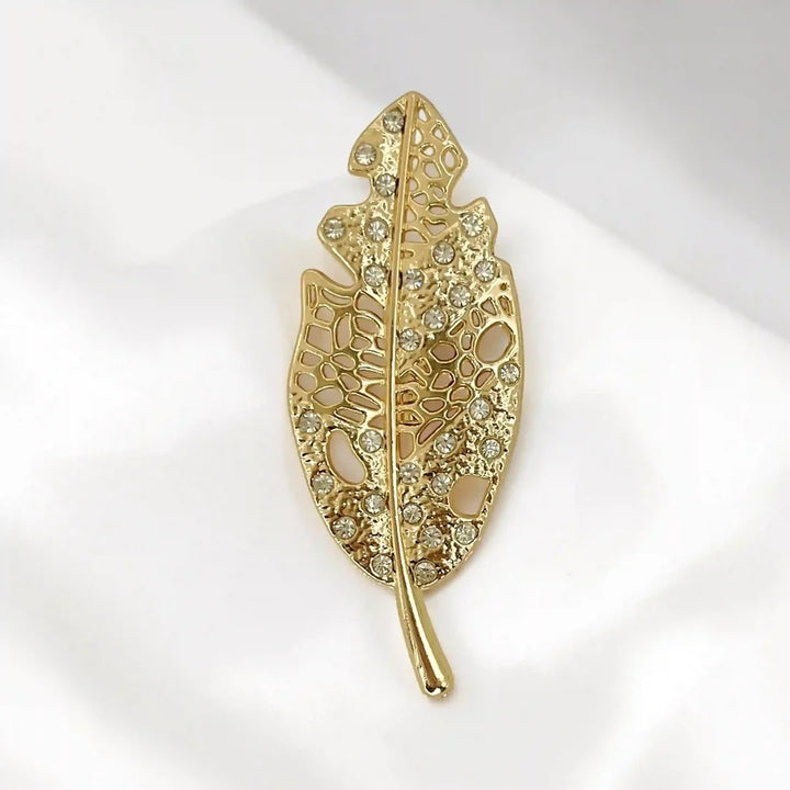 ANI Accessories gold leaf brooch with openwork design and clear rhinestones on white satin with white color background 