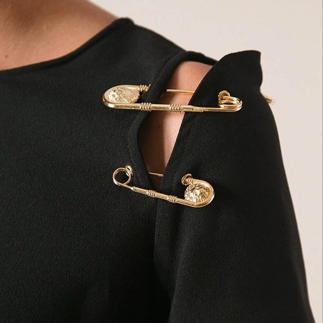 Gold lion head safety pins styled on the shoulder of a black top with white color background 