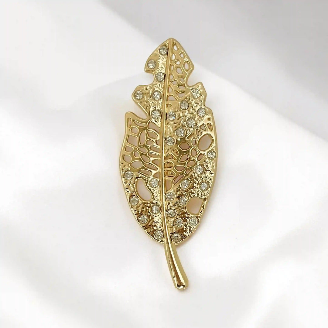 ANI Accessories leaf style metal brooch with filigree openwork and rhinestones on white satin with white color background 