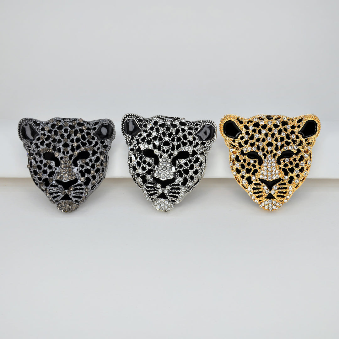 ANI Accessories leopard head brooches in gunmetal, silver and gold placed side by side on a light background 