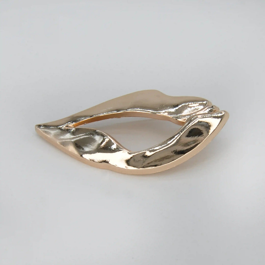 ANI Accessories lips inspired brooch in high-shine gold with a molten, rippled surface, on grey 