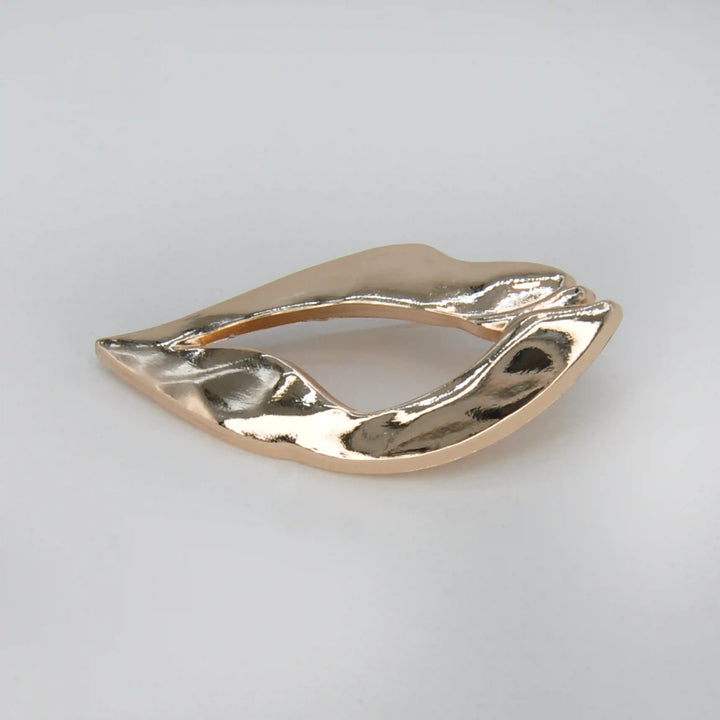 ANI Accessories lips inspired brooch in high-shine gold with a molten, rippled surface, on grey 
