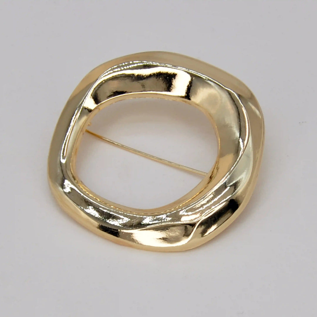 ANI Accessories organic wavy circle brooch in high-shine gold with an open centre, on grey 