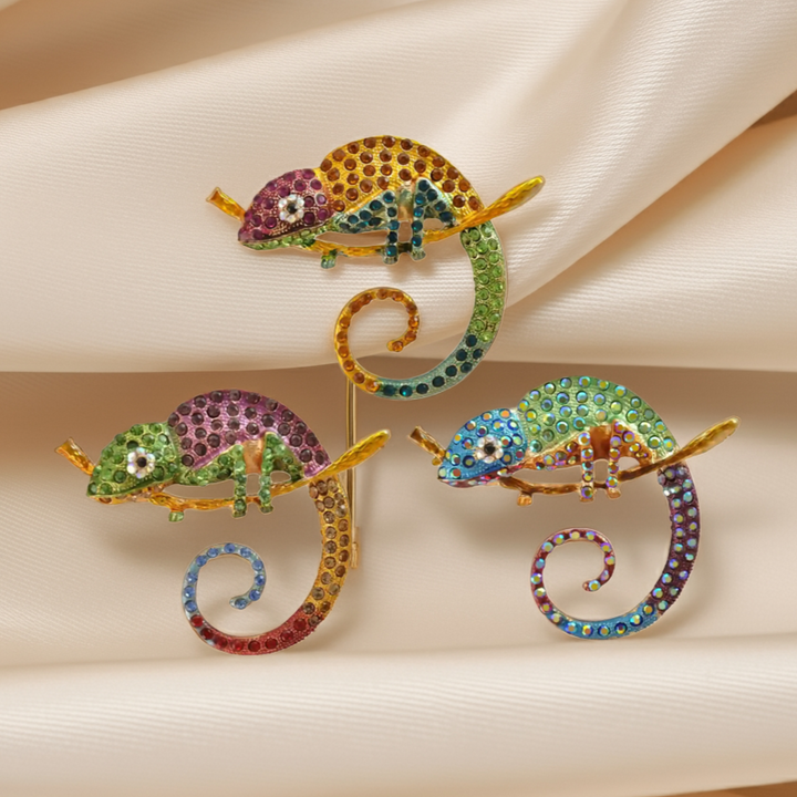 Rainbow chameleon brooches in pink, green and blue rhinestones on cream satin with white color background 