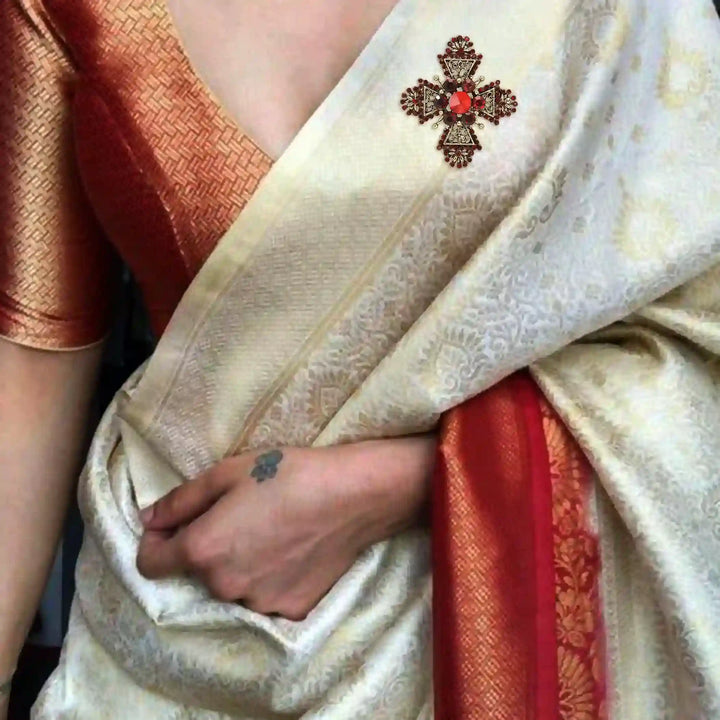 ANI Accessories red cross brooch on the shoulder of a cream saree with a red border 