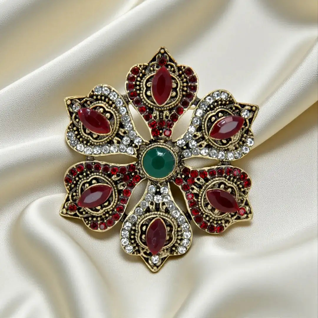 ANI Accessories red stone corsage brooch in antique gold with ruby-red stones and a green centre on satin 