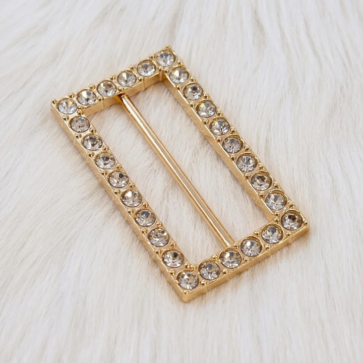 ANI Accessories rectangular rhinestone gold belt buckle, angled view of prong-set stones and raised gold frame on white fur Background 