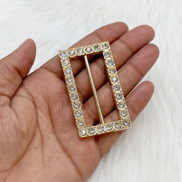 ANI Accessories rectangular rhinestone studded gold belt buckle held in palm to show real size, on white fur background