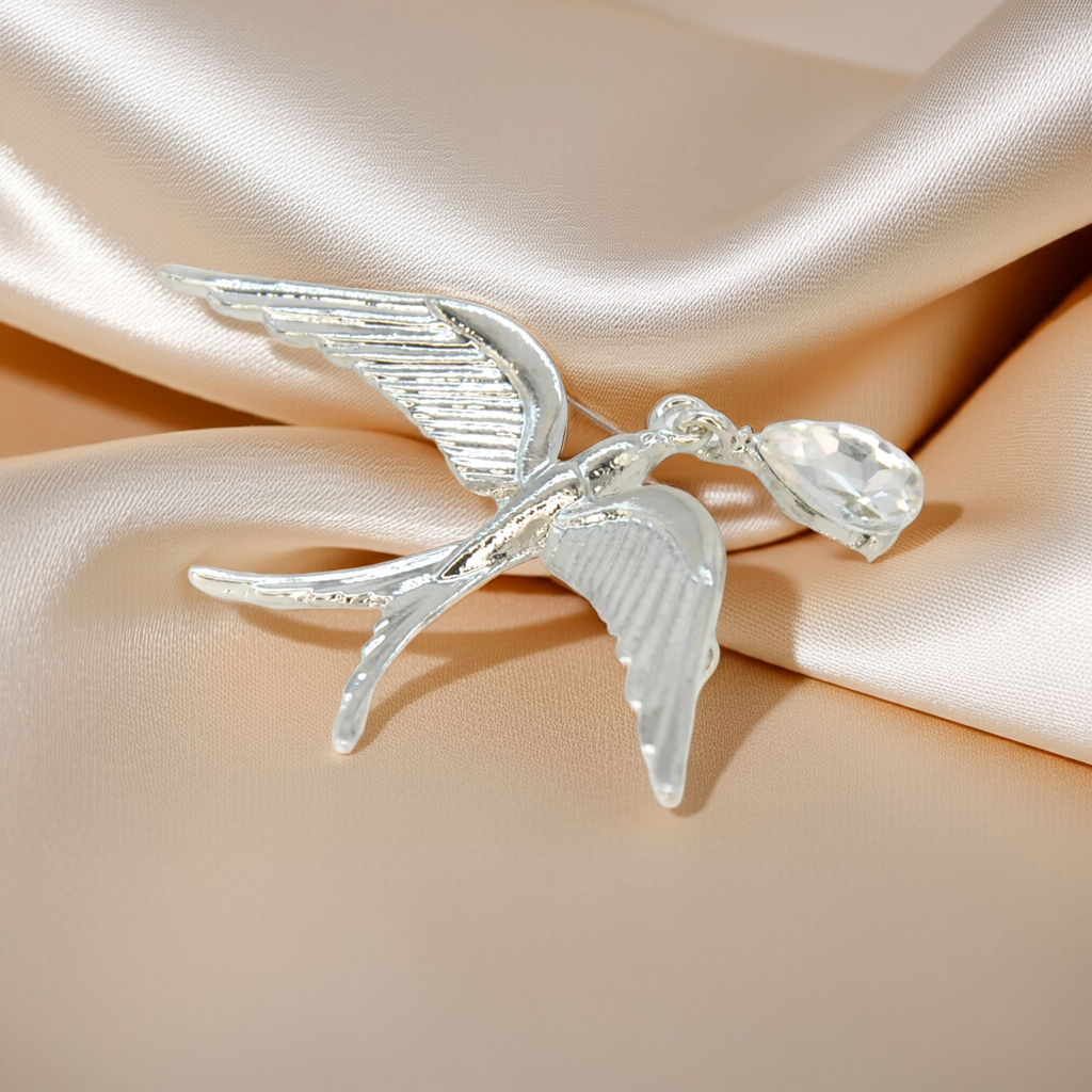 Silver swallow brooch in flight with a teardrop crystal on beige satin 