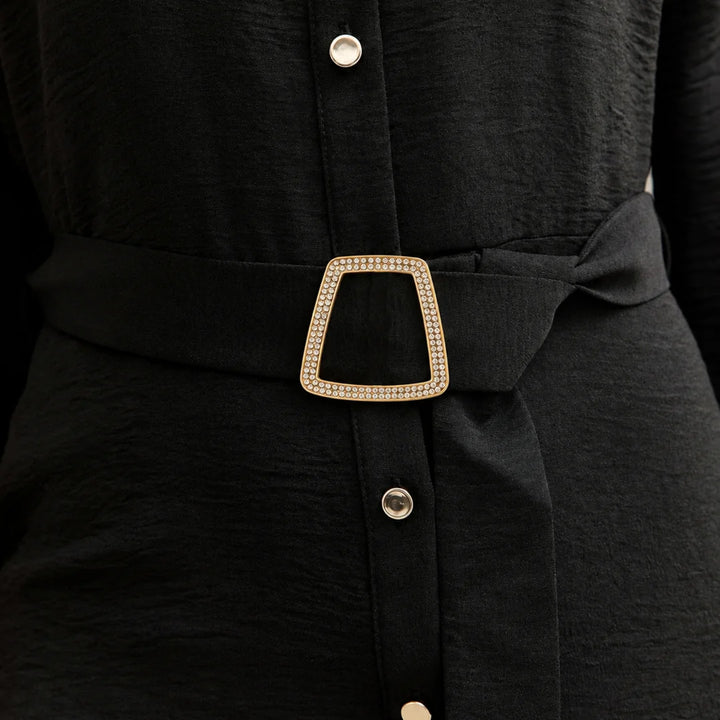 ANI Accessories trapezoid rhinestone gold buckle styled on the fabric waist belt of a black button-front shirt dress